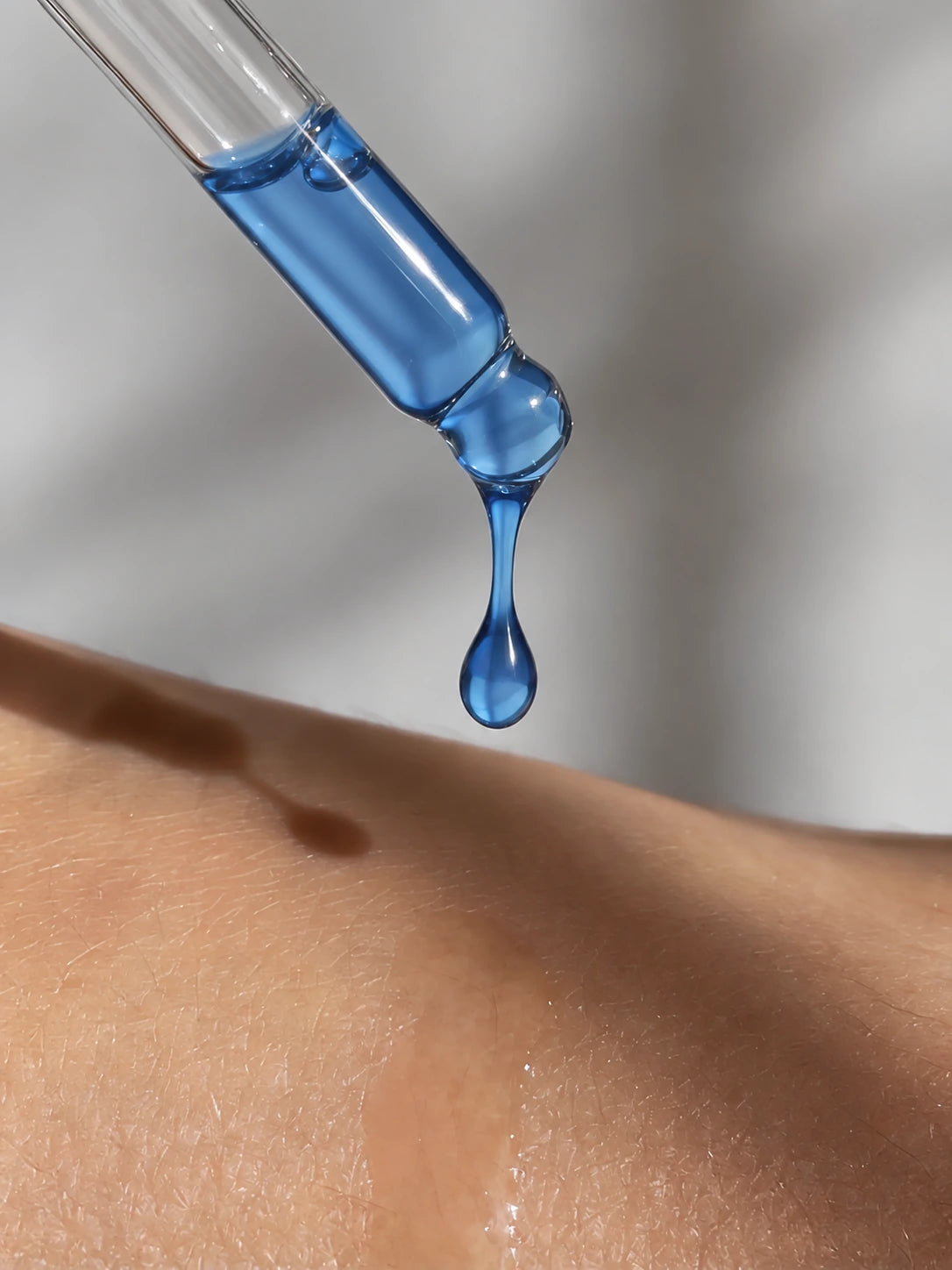 Blue GHK-Cu serum dropping from a glass pipette onto skin