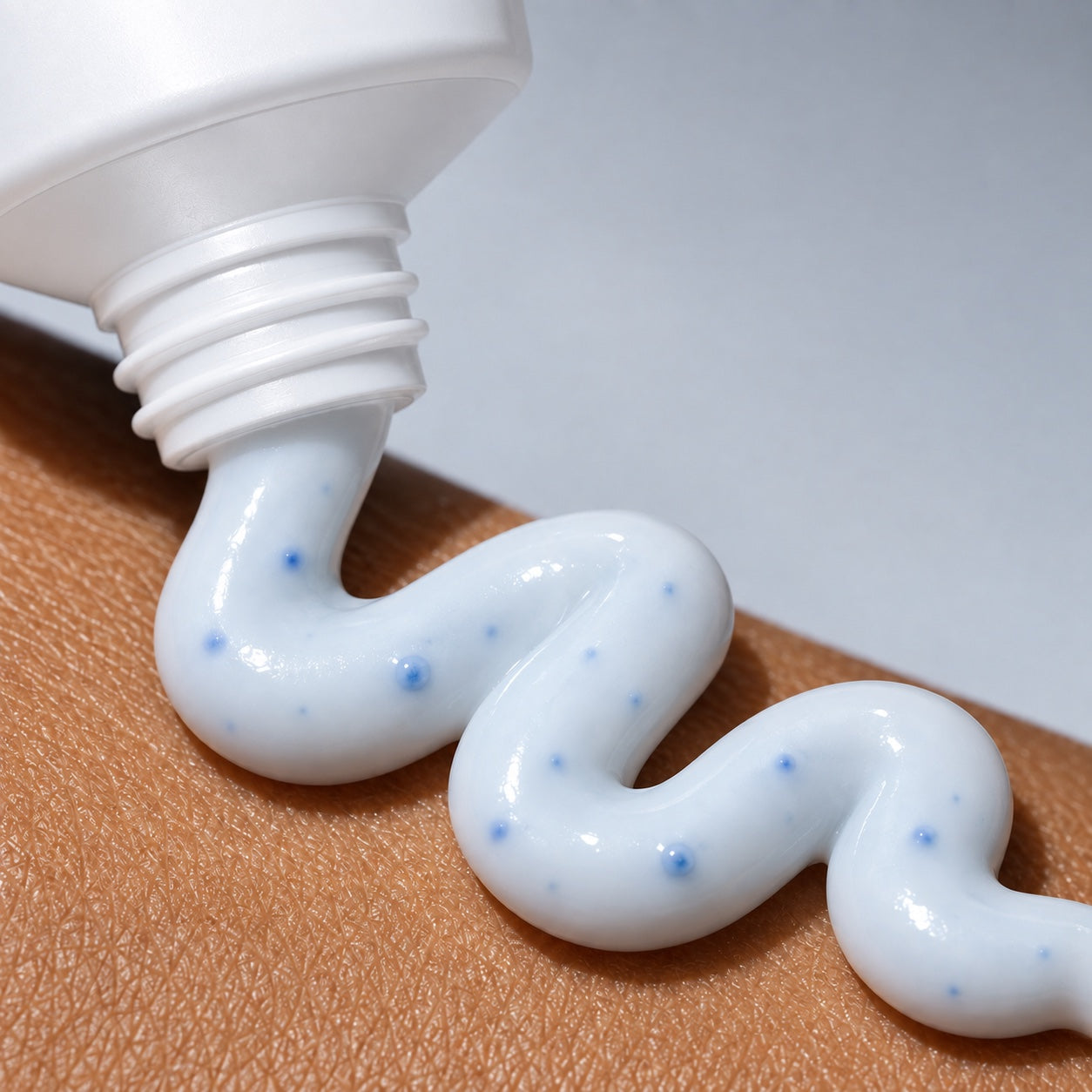Pale blue capsule cream dispensed from a white tube in a wavy line on skin