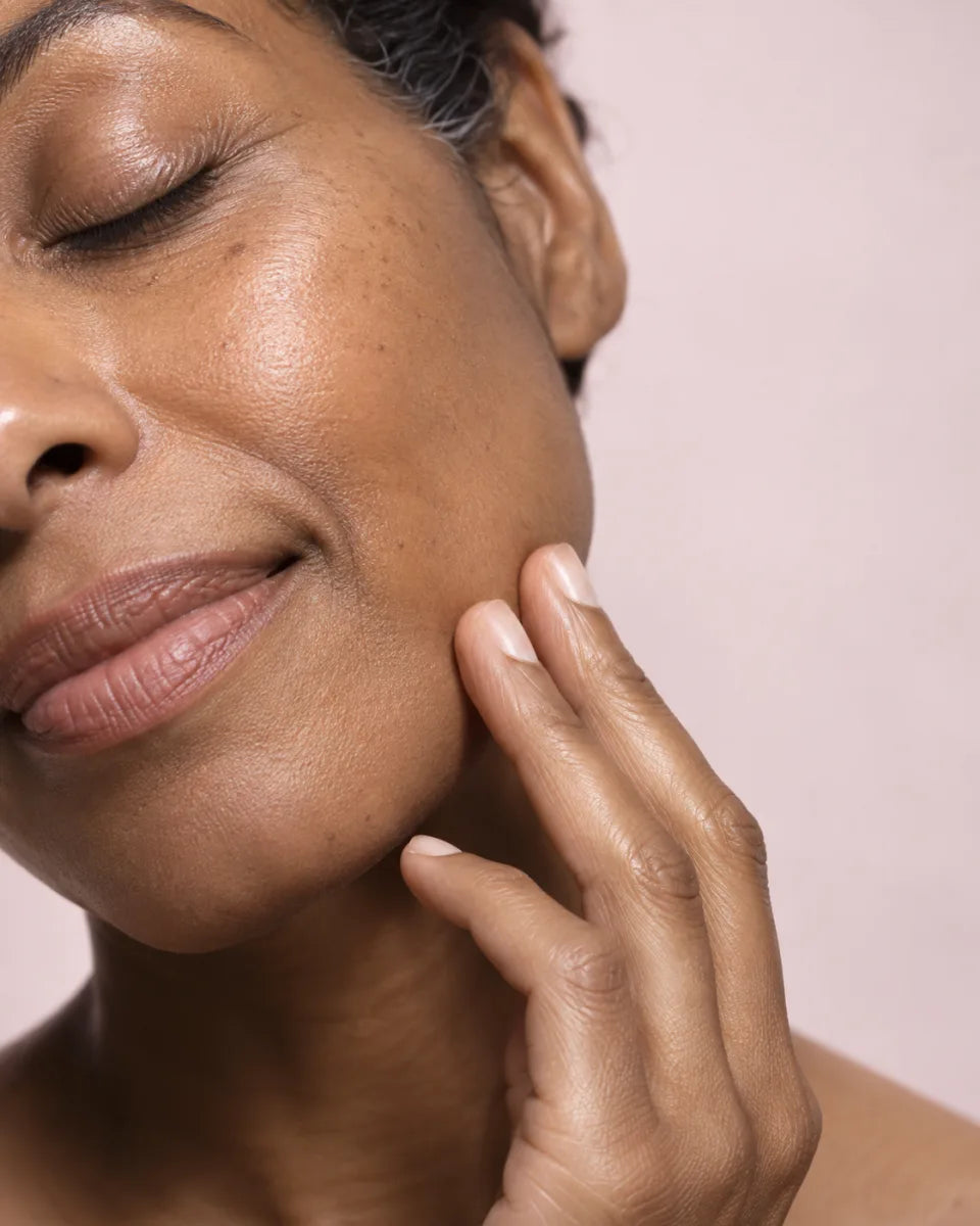 Macro portrait of a woman resting her fingertips on her cheek against a soft pink background