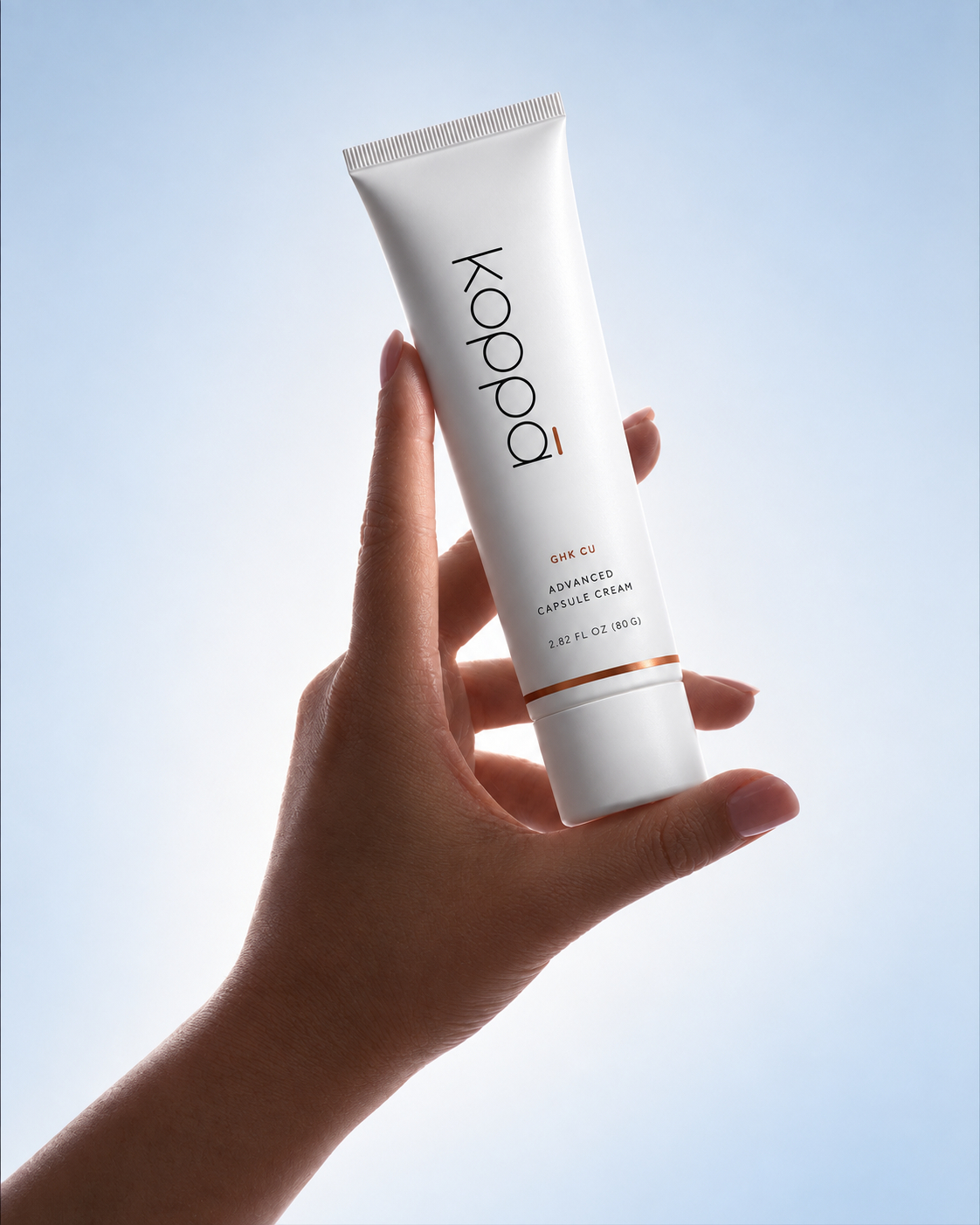 A hand holding Koppā Advanced Capsule Cream against a softly lit blue-gray background.